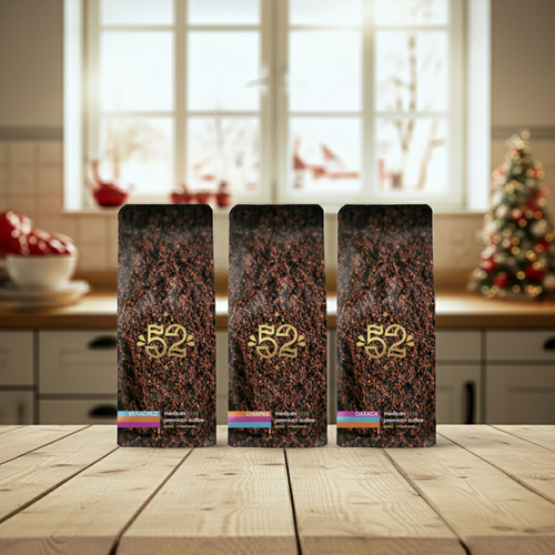Three coffee packages with a brand logo on a wooden table in a kitchen setting.